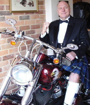 MC and entertainer Keith King from England sitting astride a Harley Davidson motorcycle, dressed in the Italian National Tartan